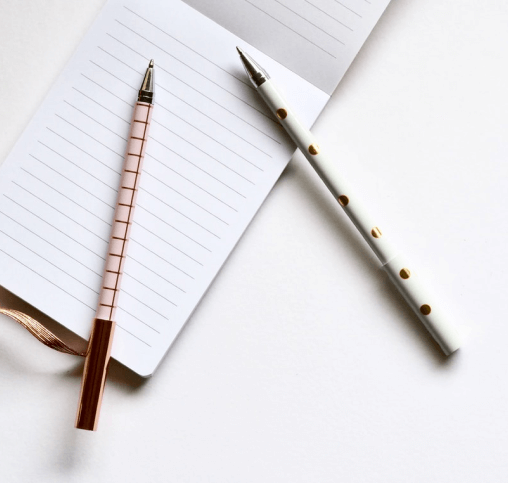 Pens and a notepad on a white surface